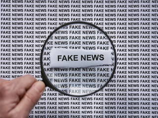 A person with a magnifying glass in his hand magnifying the words Fake News on a newspaper print background. Close up.
