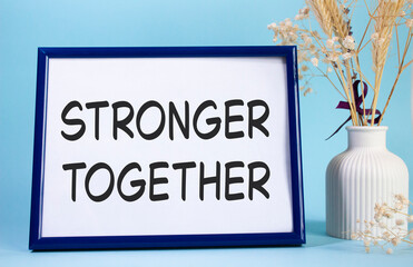 Stronger together symbol. Concept words Stronger together on beautiful wooden picture frame. Beautiful light blue background with flower vase. Business and Stronger together concept. Copy space.