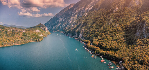 Drina river canyon with houseboats and a boat creating trails of white wake on blue water along forested mountains