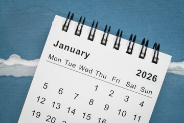 January 2026 - small spiral desktop calendar against art paper abstract, time and business concept