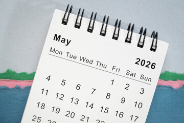 May 2026 - small spiral desktop calendar against art paper abstract, time and business concept