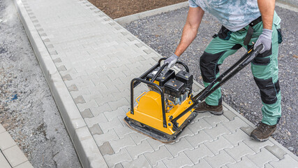 Working with vibro-compaction plate to compact self-locking blocks in their laying bed. Vibrating plate in construction.