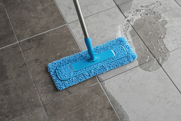 cleaning a ceramic tile floor with a mop in a home or commercial interior, demonstrating floor maintenance, hygiene, and household chores.