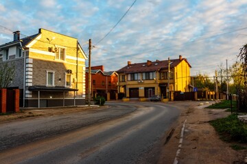 Suburban road gracefully curves past sun-kissed homes bathed in golden hour glow. Empty street...