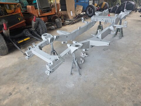 Freshly painted vehicle chassis frame supported on jack stands in a garage, surrounded by tools and parts during restoration or assembly.