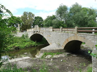 Fototapeta premium Historic Marienthal Bridge with two arches over a stream, surrounded by trees and shrubs. Copyspace.