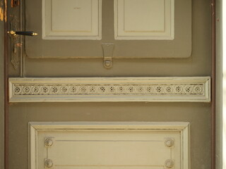 Old green wooden door with decorative strip and rosette ornaments. Chipped paint and wear visible. Close up. Copyspace.