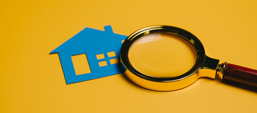 Blue house cutout with magnifying glass on yellow background symbolizing property search and inspection