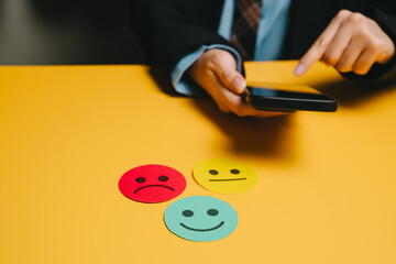 Feedback concept. Customer feedback concept with colorful emoticon faces and person holding smartphone on yellow table