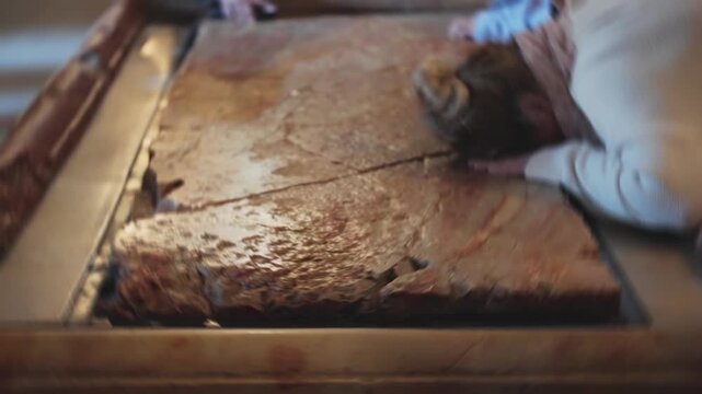Female pilgrim pray on the stone of anointing in church of the holy sepulchre. Visiting in holy land city of Jerusalem tourists and pilgrims pray and touch ancient sacred site with hope and faith