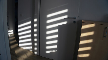 Soft shadow of window frame cast on white door and wall. Sunlight creating geometric light and shadow pattern indoors, minimalist interior detail, cozy home atmosphere still life.