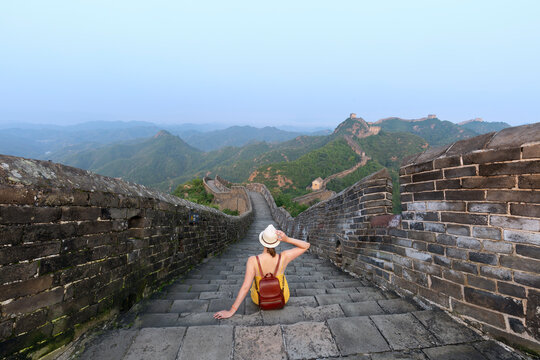 A backpacker sitting on the Great Wall in Beijing's famous Badaling area. A tourist lifestyle for a summer vacation in Asia. View of the mountain landscape. - Powered by Adobe