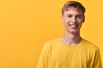 Smiling young man in a yellow shirt against a bright yellow backdrop, projecting cheerful energy,...