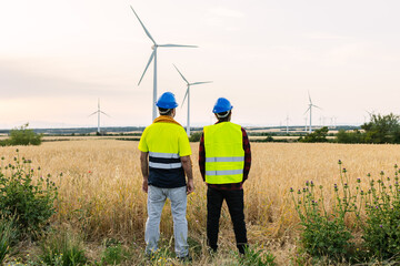Workers discussing renewable energy production in large wind farm field. Sustainability, clean power, and environmental innovation. Renewable energy and industrial workforce concept