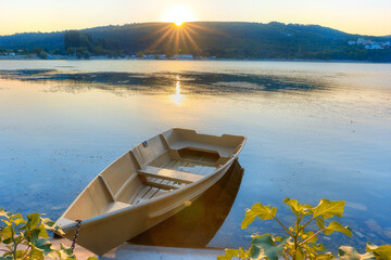 Obraz premium A boat on the shore of Lake Abrau-Dyurso in the rays of the rising sun. A beautiful summer sunrise on the lakeshore.