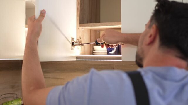 Man repairs kitchen cabinet using a screwdriver in a modern kitchen