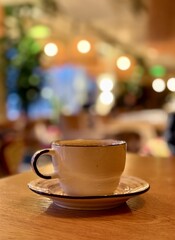 Obraz premium Ceramic Coffee Cup On Wooden Table, Creamy Crema Visible, Blurred Cafe Background With Warm Lights, Inviting Atmosphere And Shallow DepthofField For Focused Beverage Shot