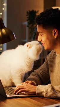 Man working on laptop with white cat at home office desk.