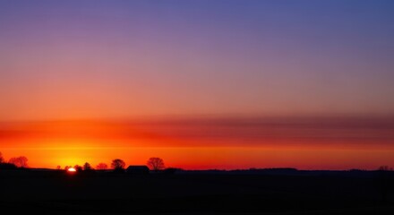 Golden hour sunset illuminates the peaceful rural landscape. Silhouettes of trees and structures stand against the vibrant, dramatic sky as twilight descends, golden hour, evening, Sunset