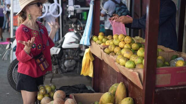 Mature woman explores a street market in Granada Nicaragua to buy fresh fruits and interact with local vendors.