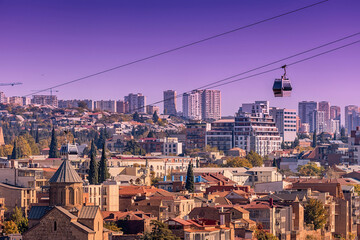 Tbilisi cityscape with cable car passing over traditional architecture and modern buildings under a purple sky