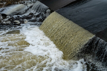 Flowing water over a small river weir creating foam and turbulence. Close-up of a hydraulic structure showing water movement, river dynamics, and human-made water management infrastructure