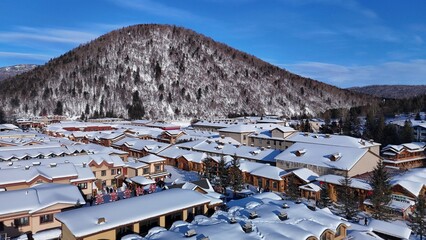 The view of the Snow Town valley in Harbin, China, is accompanied by a snowstorm, with snow clinging to the rooftops of houses, along with views of the mountains surrounding the village.