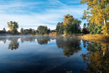 Autumn lake landscape with trees reflected in calm water at sunrise