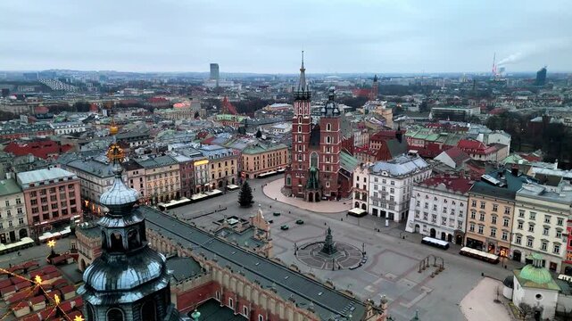 Drone footage panning left past the medieval Town Hall Tower towards the vast Rynek Gł&oacute;wny, showcasing Sukiennice and St. Mary's Basilica at sunrise in Krakow, Poland.