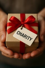 Person's hands carefully holding a small gift box with a charity tag and red ribbon for thoughtful giving concept and corporate social responsibility