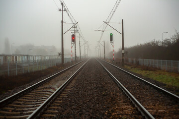 Railway tracks disappearing into fog with red and green railway signals. Moody scene symbolizing transportation, direction, safety, decision making, and uncertainty in an overcast landscape