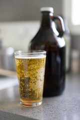 A freshly-poured glass of beer sits on a counter top next to a glass growler.