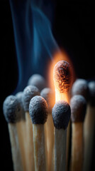 Ignited match among unlit matches on dark background creating blue smoke