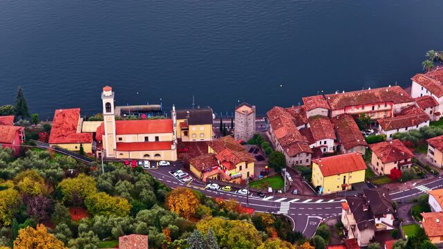 Aerial overview of town center along Lake d&rsquo;Iseo with dense rooftops and shoreline development, tracking left, vibrant red roof