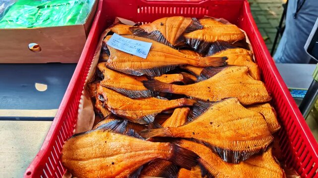 Smoked flatfish with golden-brown skin piled inside a bright red plastic crate at a market