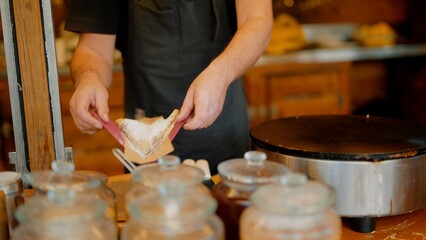 Busy street food vendor preparing warm crepes for takeaway