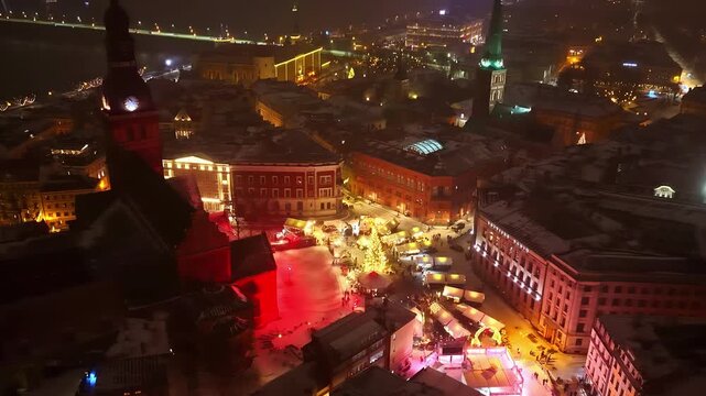 Nighttime aerial of Riga Christmas market in Doma Square with church towers and snowy rooftops