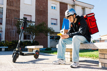 Young delivery boy with electric scooter and smartphone