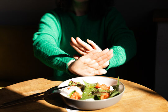 Hands gesture to refuse a healthy salad on a wooden table