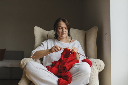 Woman knitting a red sweater in a cozy chair