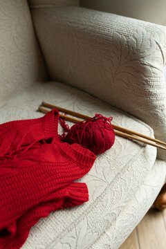 Knitting hobby with red sweater on comfortable armchair
