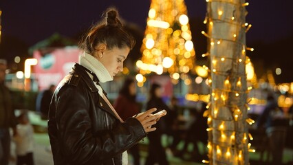 Woman wearing leather jacket browsing on her mobile phone at night