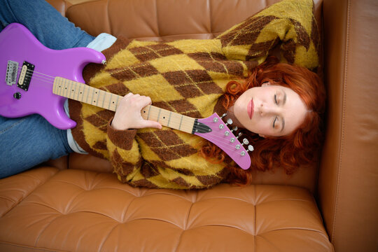 Relaxed woman lying with guitar on leather sofa