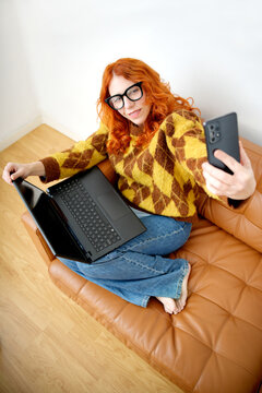Woman taking selfie while sitting on couch with laptop