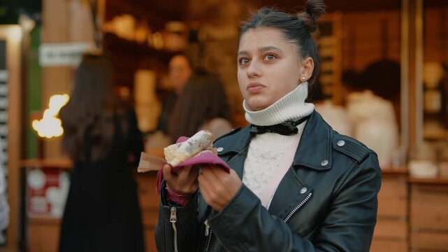 Vivid scene of woman pausing to savor delicious crepe at bustling market