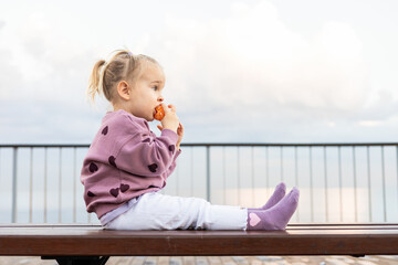 Toddler enjoying a snack on a bench at sunset