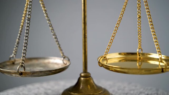 Close-up of an antique brass balance scale with silver and gold pans resting on a marble surface against a gray background. Symbolizing justice and law.
