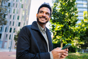 Portrait of smiling young adult man holding smartphone outdoors. Natural expression while enjoying digital interaction outdoors. Technology and lifestyle concept.