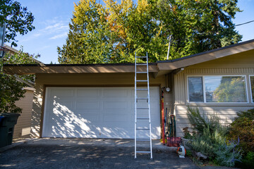 Fall home maintenance, ladder leaning against roof ready to clean climb and clean gutters
