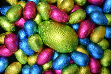 Pile of colourful foil wrapped chocolate easter eggs in pink, blue, yellow and lime green with a large green egg in the middle.